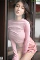 A woman in a pink shirt is posing by a window.