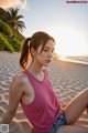 A woman in a pink tank top sitting on a beach.