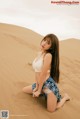 A woman sitting on top of a sand dune in the desert.