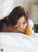 A woman laying on a bed holding an orange.