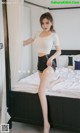 A woman in a white top and black shorts posing on a bed.