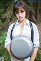 A woman in a white shirt and black suspenders holding a frying pan.