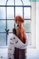 A woman with long red hair standing in front of a window.