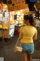 A woman in shorts and a yellow shirt is walking down the street.